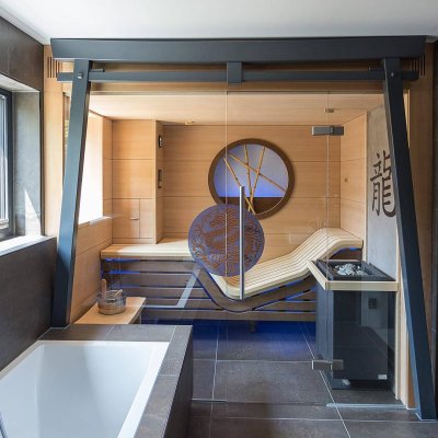 Eingebaute Saunakabine mit Torii-Tor-Element in einem dunkel gefliesten Wellnessraum